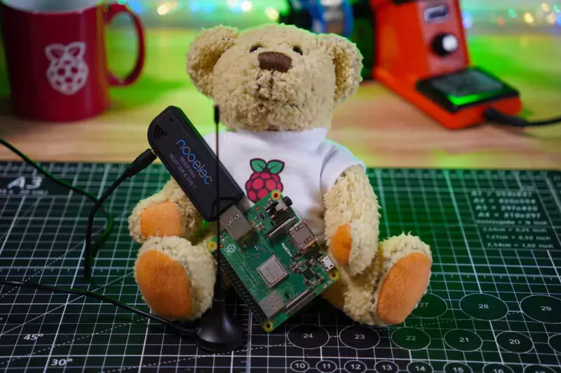 Babbage Bear holding a Raspberry Pi 3 Model A+ attached to flight tracking hardware
